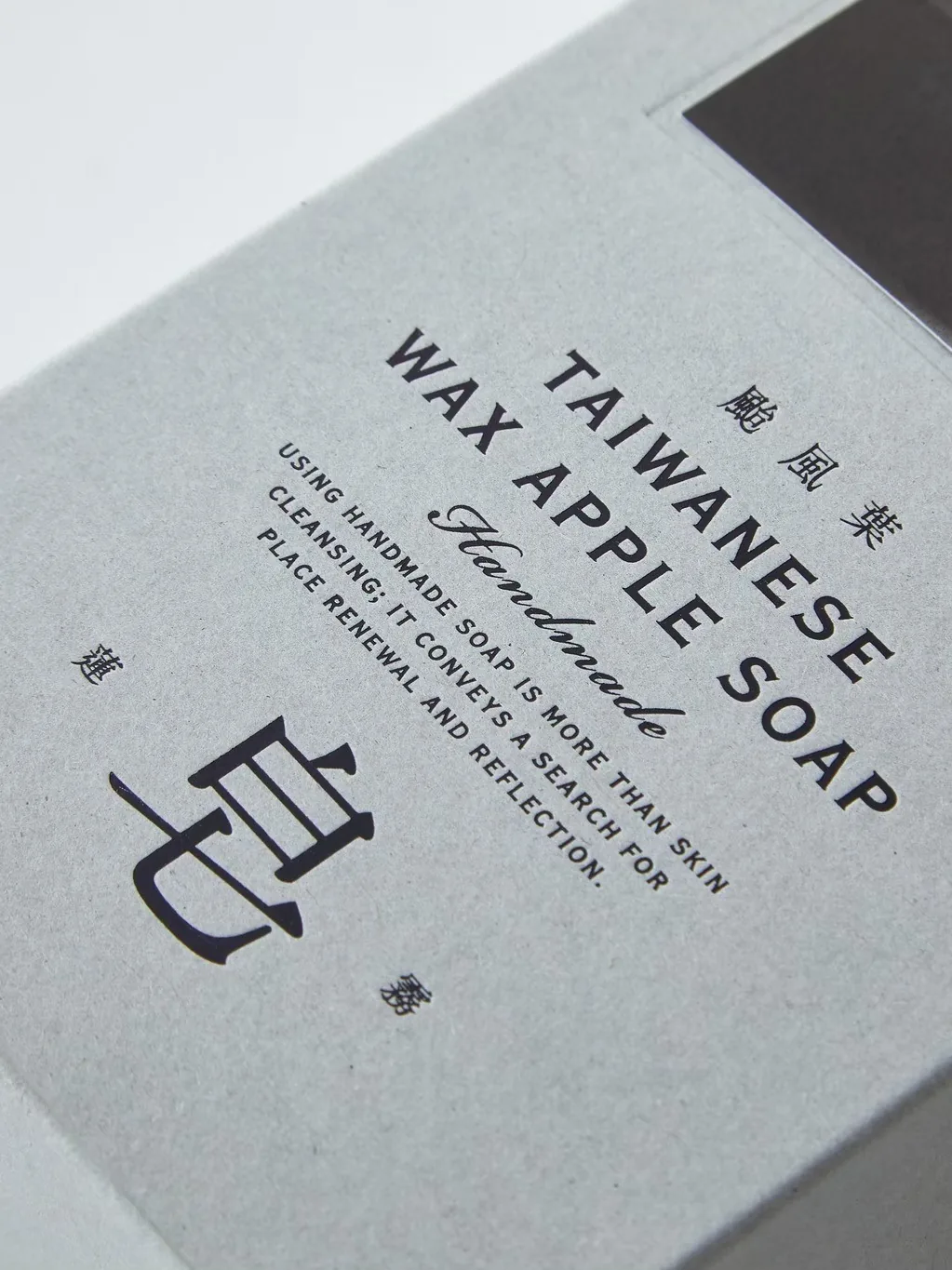 颱風葉蓮霧皂的灰色紙盒特寫，印著 TAIWANESE WAX APPLE SOAP 與「皂」字
